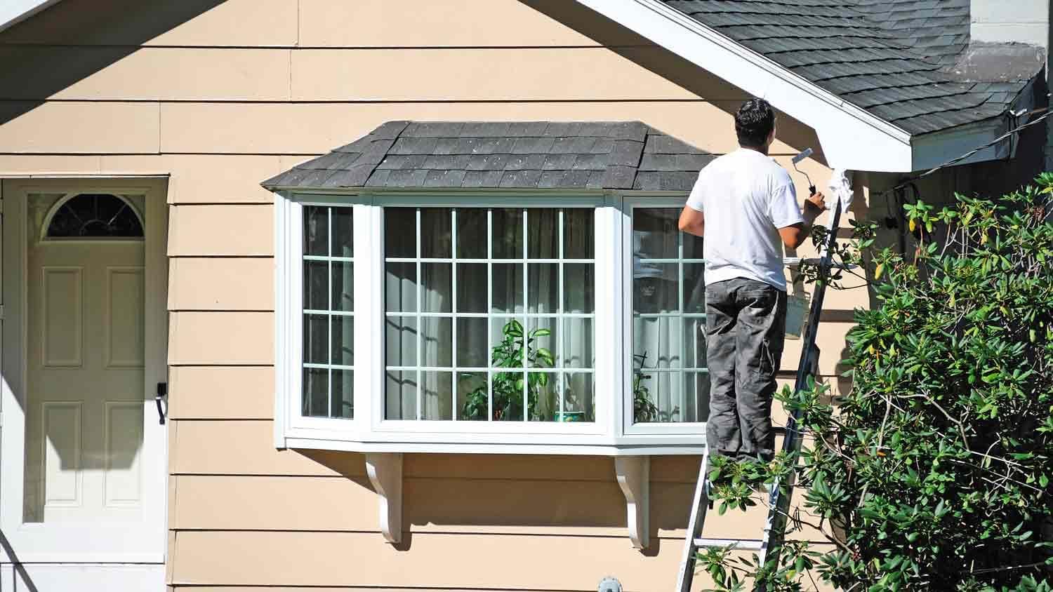 A worker on a ladder beside a bay window